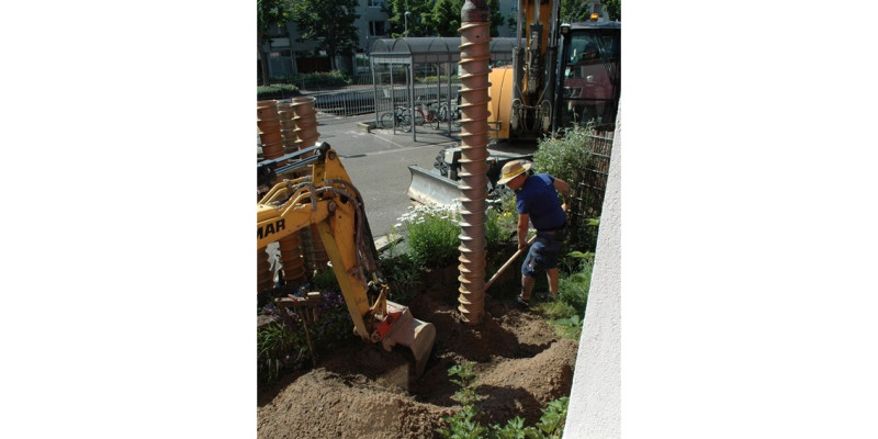 Bohrungen von Erdsonden im Vorgarten: Man sieht den Bohrer, einen Bagger und einen Arbeiter.