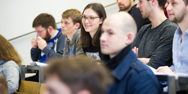 Ein kleinerer Bildausschnitt von Studierenden im Hörsaal. Eine Person im Bildzentrum sagt etwas, andere hören zu und schauen sie dabei an oder nach vorne.