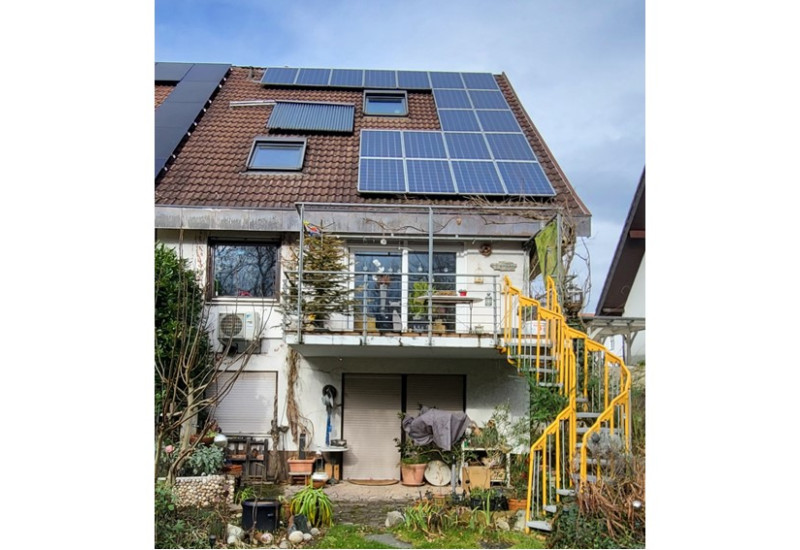 Ein zweistöckiges Haus mit Photovoltaik und Solarthermie auf dem Dach. Im Vordergrund der Garten.