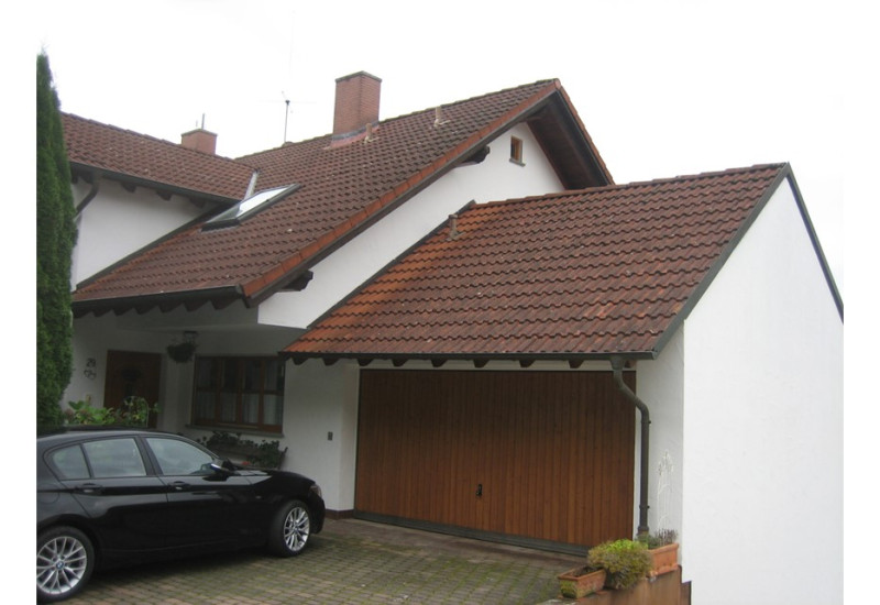 Doppelhaushälfte von der Straßenseite aus gesehen; im Vordergrund die Garage mit Auto in der Einfahrt